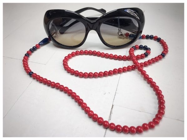 A chain for glasses made of red stones with navy blue accessories on a linen bag.