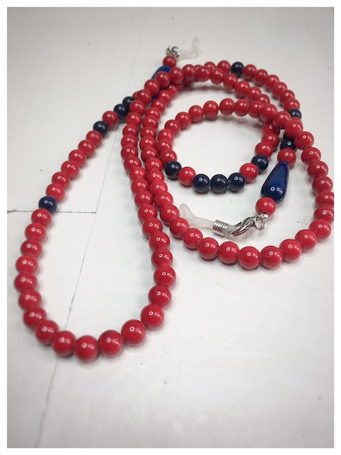 A chain for glasses made of red stones with navy blue accessories on a linen bag.