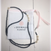 A chain for glasses made of black stones with cream roses and pebbles between them on a linen packaging bag.