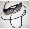 A chain for glasses made of black stones with cream roses and pebbles between them on a linen packaging bag.