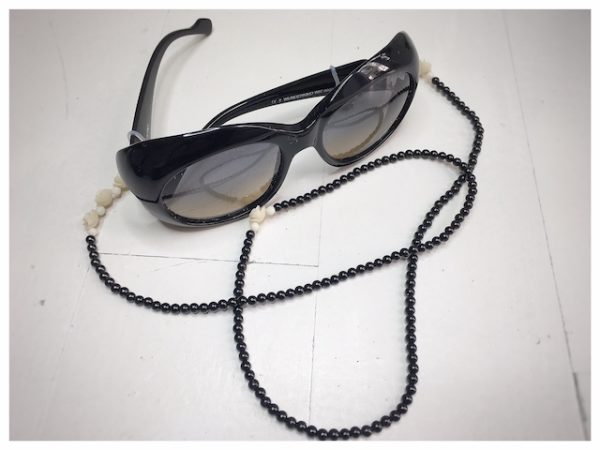 A chain for glasses made of black stones with cream roses and pebbles between them on a linen packaging bag.