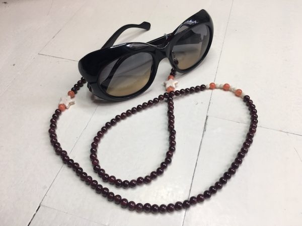 A chain for glasses made of maroon stones with beige stars between orange stones.