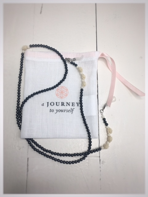 A chain for glasses made of black stones with cream roses and pebbles between them on a linen packaging bag.