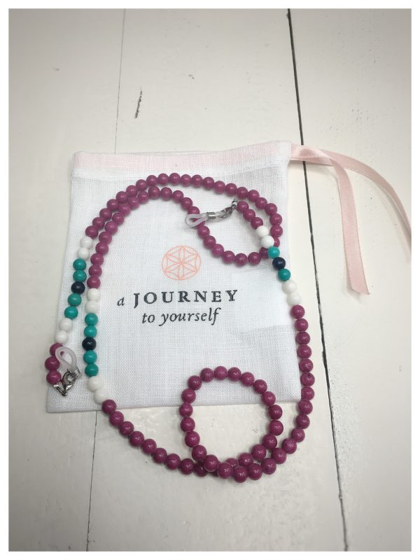 A chain for glasses made of fuchsia-colored stones with white and turquoise accessories on a linen packaging bag.