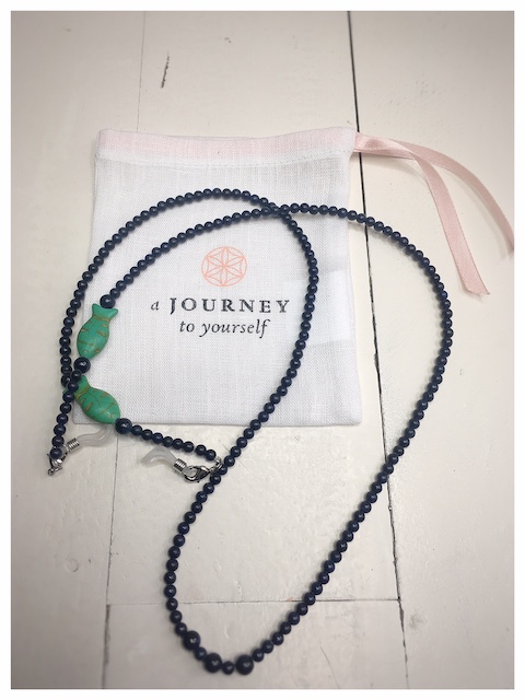 A chain for glasses made of navy blue stones with green fish on a linen packaging bag.