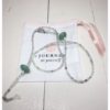 A chain for glasses made of celadon-violet glass stones with a celadon larger stone on a linen packaging bag.