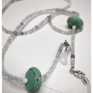 A chain for glasses made of celadon-violet glass stones with a celadon larger stone on a linen packaging bag.