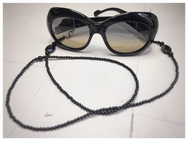 Łańcuszek do okularów z kamieni koloru czarnego na lnianej torebce opakunkowej.