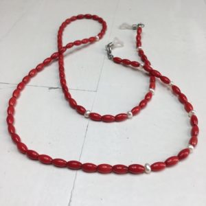 Łańcuszek do okularów z kamieni koloru czerwonego z perełkami pomiędzy nimi na lnianej torebce opakunkowej.