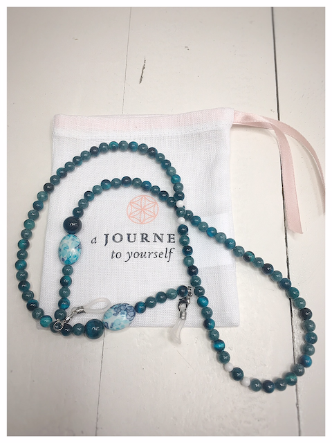A chain for glasses of turquoise color with a white-turquoise larger stone on a linen packaging bag.