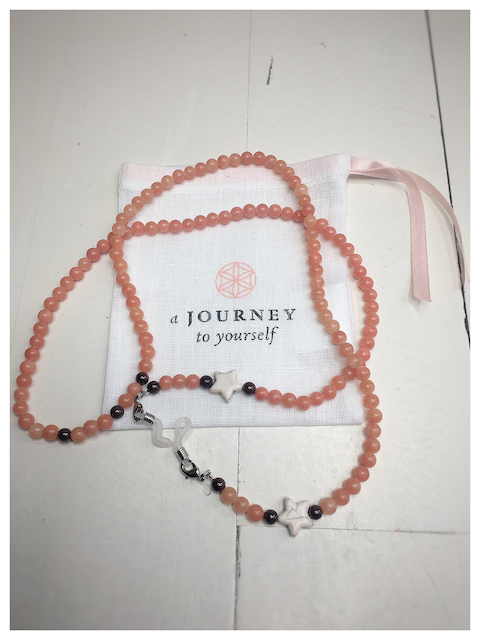 An orange eyeglass chain with a beige star and dark beads around it on a linen wrapping bag.