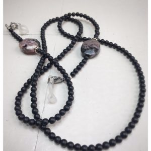 A chain for glasses made of black stones with one larger purple-black stone on a linen packaging bag.