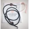 A chain for glasses made of black stones with one larger purple-black stone on a linen packaging bag.