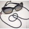 A chain for glasses made of black stones with one larger purple-black stone on a linen packaging bag.