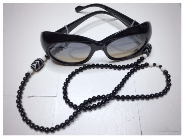 Łańcuszek do okularów „Wzmocnienie” to obrazek łańcuszka z kamieni naturalnych w kolorze czarnym z białymi dodatkami z okularami.